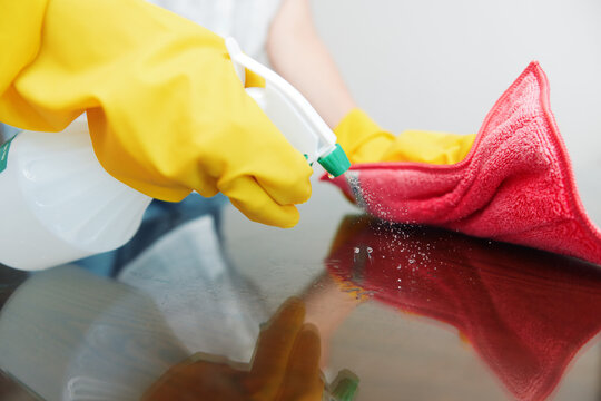 Woman in yellow gloves cleaning table with rag and cleaning solution bottle