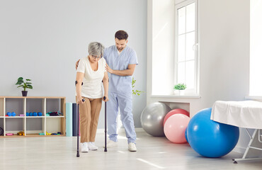 A doctor at a rehabilitation center helps an elderly woman walk on crutches. Concept of the recovery process after surgery. Support for pensioners in a medical institution, specialized assistance