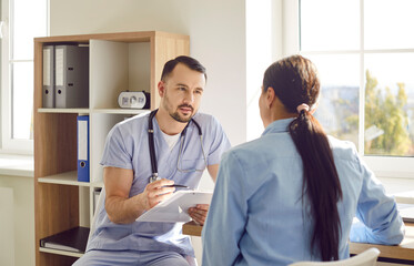 Portrait of a young woman patient in medical office listening to friendly male doctor holding...