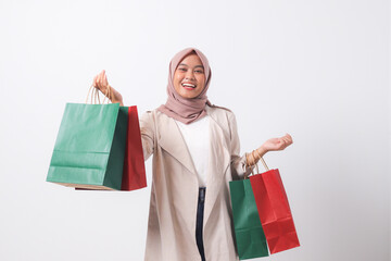 Portrait of attractive Asian hijab woman in casual suit holding and showing colorful paper shopping bags. Shopaholic girl and discount buying concept. Isolated image on white background