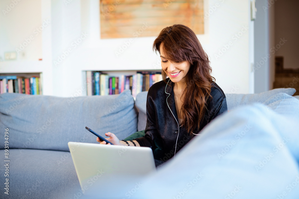 Wall mural Mid aged woman using smartphone and laptop at home