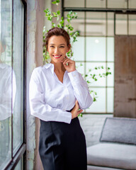 Portrait of a brunette haired woman standing at the window and smiling into the camera