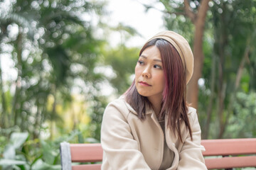 Naklejka premium Thirty-something Hong Kong woman with reddish-brown hair sitting on a bench by a large fountain in Kowloon Park, Tsim Sha Tsui, Kowloon Island, Hong Kong, during a cold winter.