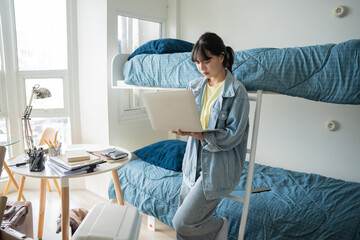 Student asian woman sitting on bed in dorm room college student Work or homework on laptop in university dormitory