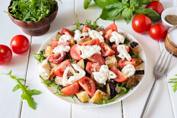 Salad with eggplant, tomatoes, arugula and strachatella on a white plate on a white background. Homemade salad for breakfast. Vegetarian dish. Close-up