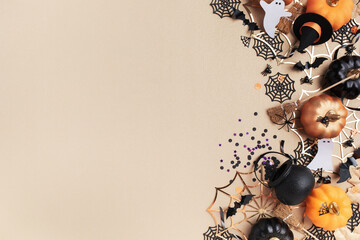 Naklejka premium Halloween holiday frame with party decorations from pumpkins, bats, spider web and ghosts top view. Happy halloween greeting card on golden background flat lay style..