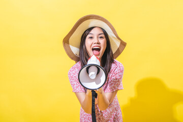 Fototapeta premium Asian woman wearing a straw hat and a pink floral dress, holding a megaphone with a shouting expression against a yellow background. The lighting style is bright and even.
