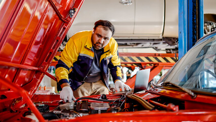 Mechanic Asian man wear uniform using computer laptop examining tuning fixing repairing car engine automobile vehicle parts using tools equipment in workshop garage support and service in overall work