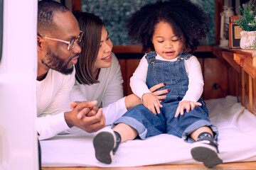 Happy multiracial family having fun relaxing together. Portrait of multiethnic father mother and little biracial daughter playing at backyard camping. Diverse ethnic dad mom leisure with afro kid