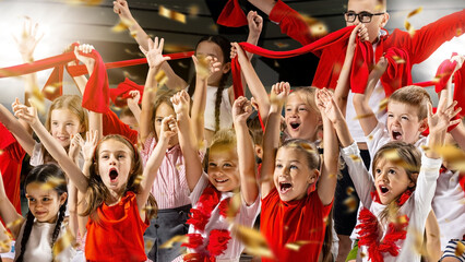 Group of excited children cheering, waving red scarves and wearing red and white outfits. Confetti fills air, capturing joy and energy of celebration. Concept of sport, match, competition, support. Ad