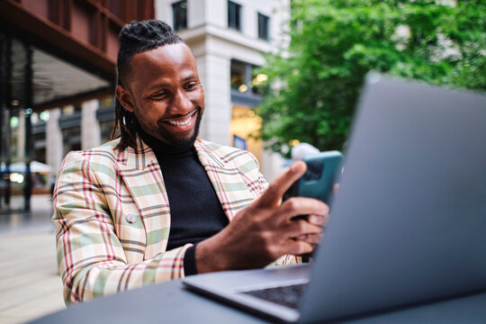 Smiling businessman using smart phone with laptop on table at sidewalk cafe