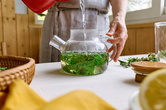 Woman pouring water in teapot mixed with herbal leaves for making tea at home