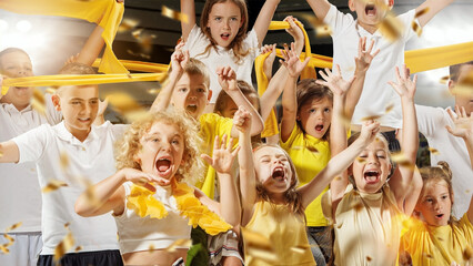 Energetic kids cheering and waving yellow scarves with golden confetti raining down around them....