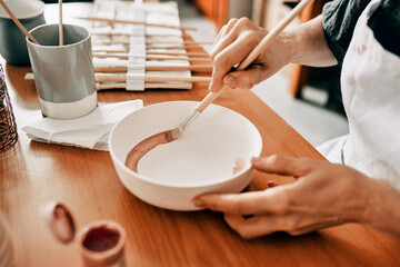 Person, hands and painting in pottery studio with creative pattern, art design and small business. Closeup, artist and color process for ceramic bowl with sculpture product, manufacturing and startup