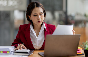 Serious and focused financial accounting on documents paper work at office, Asian woman use calculator and laptop for calculating reports and summarizing accounts, business at work in casual clothes.