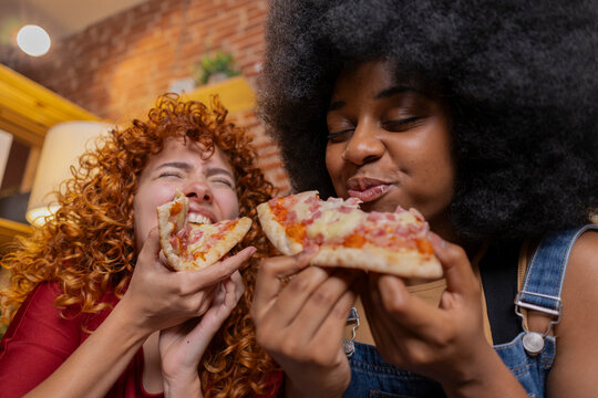 Multiracial friends eating slice of pizza at home