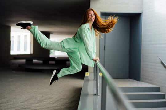 Happy redhead woman jumping from support of railing in parking garage