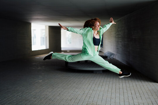 Flexible redhead woman dancing with mid-air splits at parking garage
