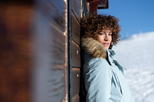 Curly hair woman in winter coat leaning on log cabin