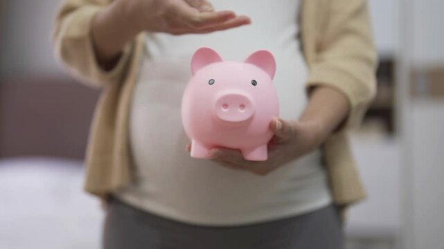 A portrait of happy Asian pregnant woman save financial money for baby with piggy bank in bedroom at home. Having a baby. Family people lifestyle. Mom love.