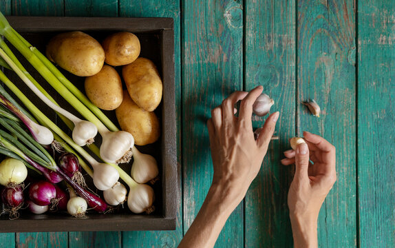 Hands of woman holding garlic next to wooden crate of vegetables on table