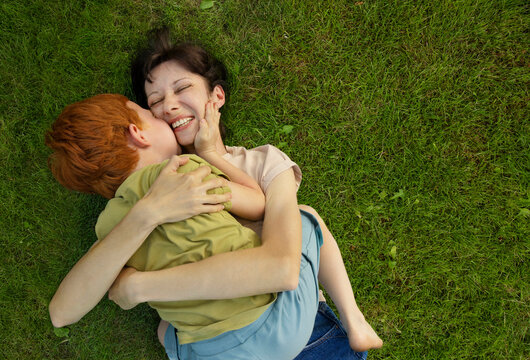 Redhead boy kissing mother lying on grass in garden
