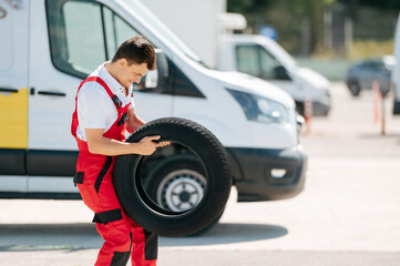 Young smiling man, in red coverall,  car mechanic holding auto tires