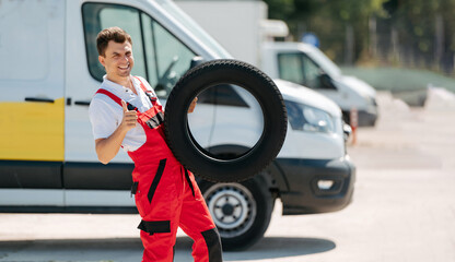 Young smiling man, in red coverall,  car mechanic holding auto tires