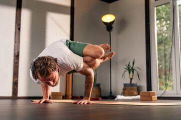 A man practicing advanced yoga pose in a serene indoor setting with natural light.