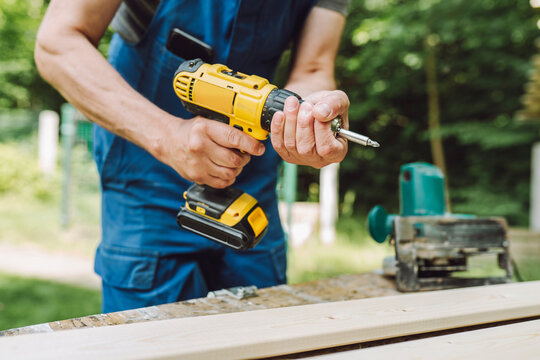 Mature man with power screwdriver near planks at back yard