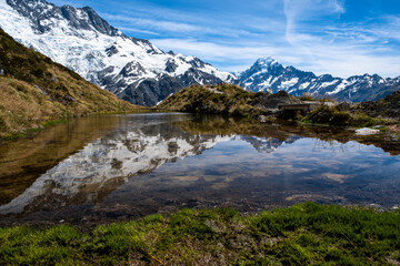 A serene alpine lake with crystal clear waters reflecting snow-covered mountains and a blue sky, creating a tranquil and picturesque scene.