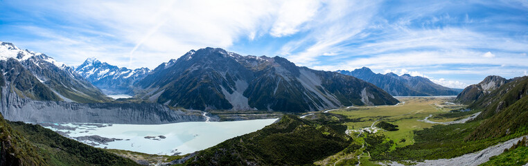 A stunning panoramic shot capturing the expansive view of snow-capped mountains and a serene lake below. The lush greenery and clear sky make it an ideal image for backgrounds and graphic designs.