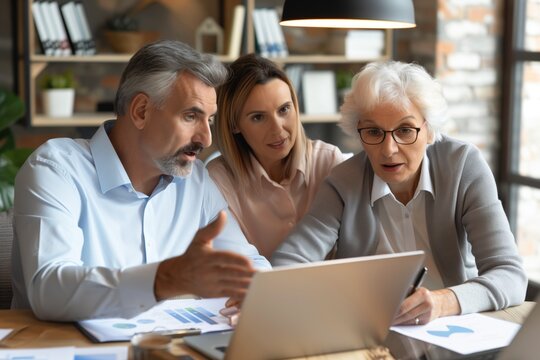 Older man presenting financial report on a laptop to senior woman and younger woman in an office. Business meeting, teamwork, financial consulting, multi-generational workplace, collaboration concept.