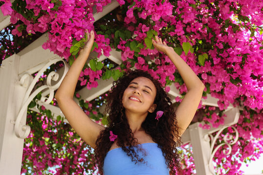 Smiling woman with arms raised at pink blooming bougainvillea vine