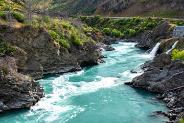 A vibrant turquoise river flows through a rugged rocky canyon surrounded by greenery, showcasing the beauty of nature.