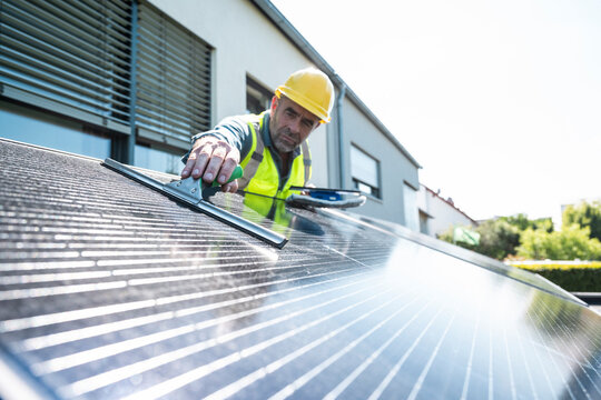 Technician cleaning solar panel on house rooftop