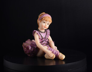 Resin figurine of a ballerina girl in purple dress, on black background.