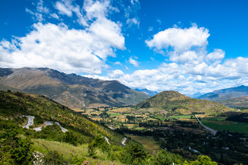 Beautiful valley landscape featuring a winding road, lush greenery, and surrounding mountains under a clear blue sky.