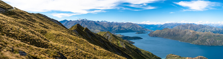 A panoramic view of a mountain ridge and lake, highlighting the vastness and beauty of the natural landscape. The clear blue sky and expansive scenery create a tranquil and inviting atmosphere.