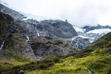A stunning view of a glacier with multiple waterfalls cascading down the rugged mountain, surrounded by vibrant green meadows.