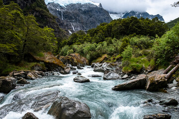 A serene river flowing through a mountain valley, with a majestic waterfall and lush forest creating a picturesque landscape.