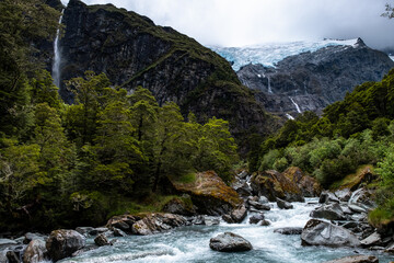 A serene river flowing through a mountain valley, with a majestic waterfall and lush forest...