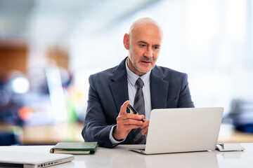 Mid aged businessman sitting at the office and using laptop while having video call