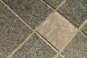 A ceramic textured tile among pebble stone floor tiles.