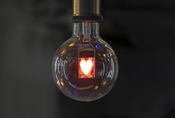 Interior of an incandescent lamp with heart-shaped filament hanging under in a shop against black background, South Korea
