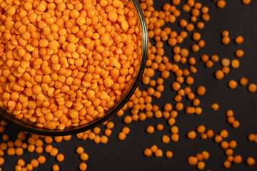 Raw red lentils are scattered out of the glass bowl