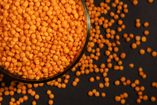 Raw red lentils are scattered out of the glass bowl