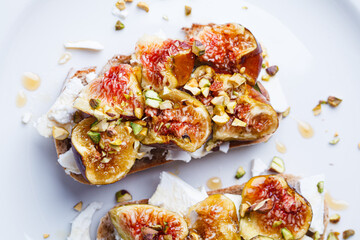 Breakfast toast with feta cheese, figs and pistachios on white plate, white background.