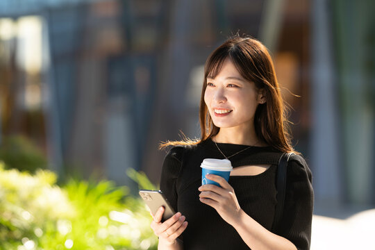 街でコーヒーとスマホを持って笑っている女性