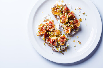 Breakfast toast with feta cheese, figs and pistachios on white plate, white background.